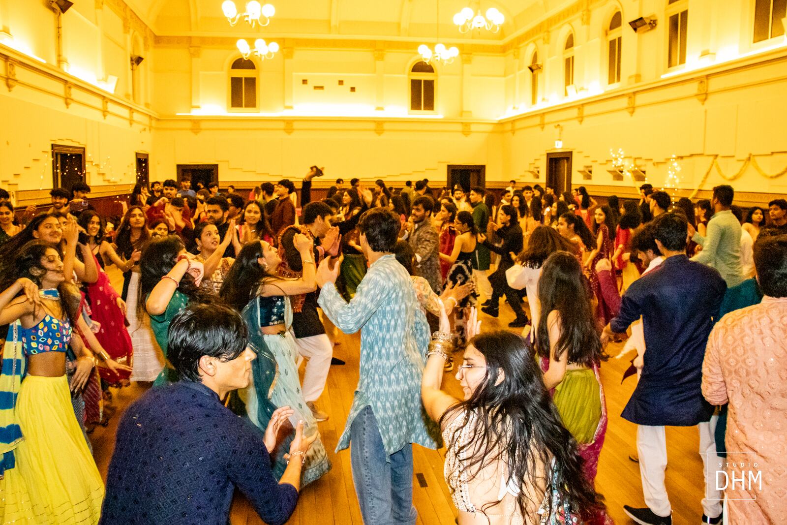 A packed hall of students dancing at a MUIC Garba night, lit in warm gold