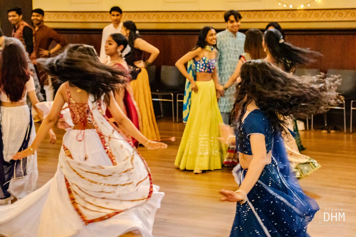 Dancers in traditional dress moving through a golden-lit Garba hall